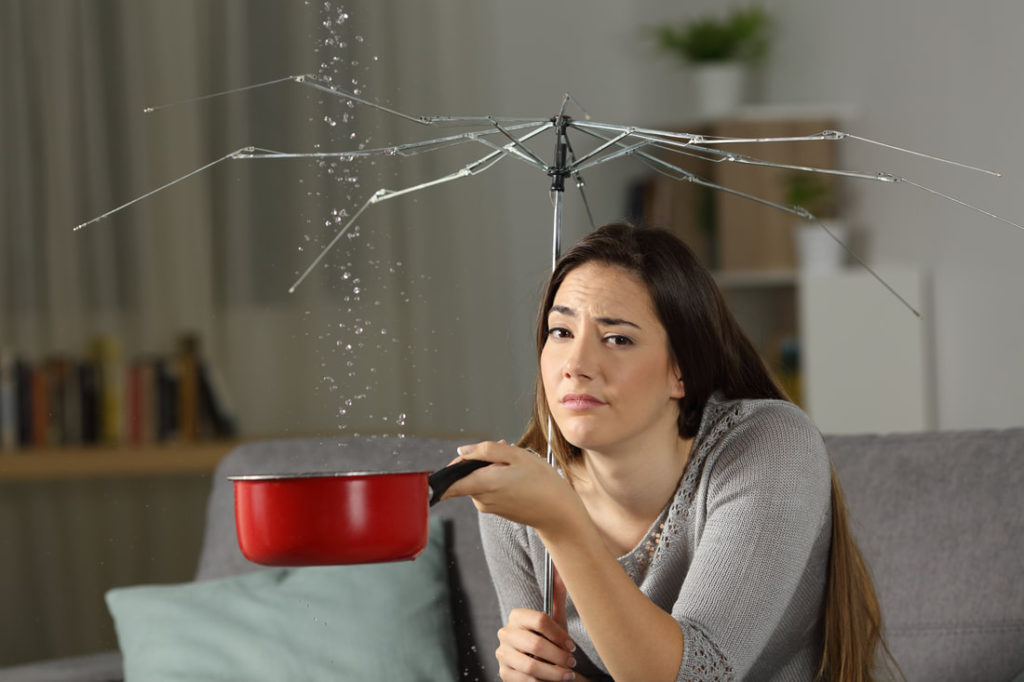 This Is A Picture Of A Women Sitting On A Couch With A Broken Umbrella With Her Ceiling Raining On Her Waiting For Plumbers Erie Pa